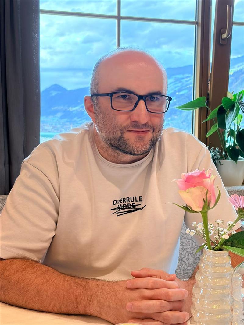 Sebastian Flack am Tisch vor einem Fenster mit Bergblick